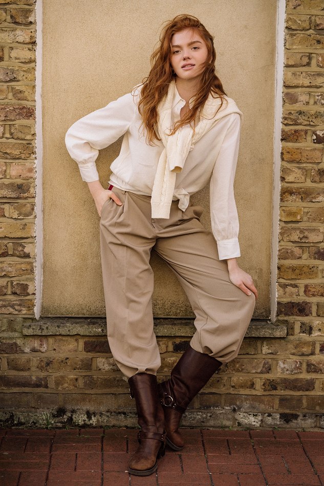 Camryn in a white shirt and tan trousers by a brick wall