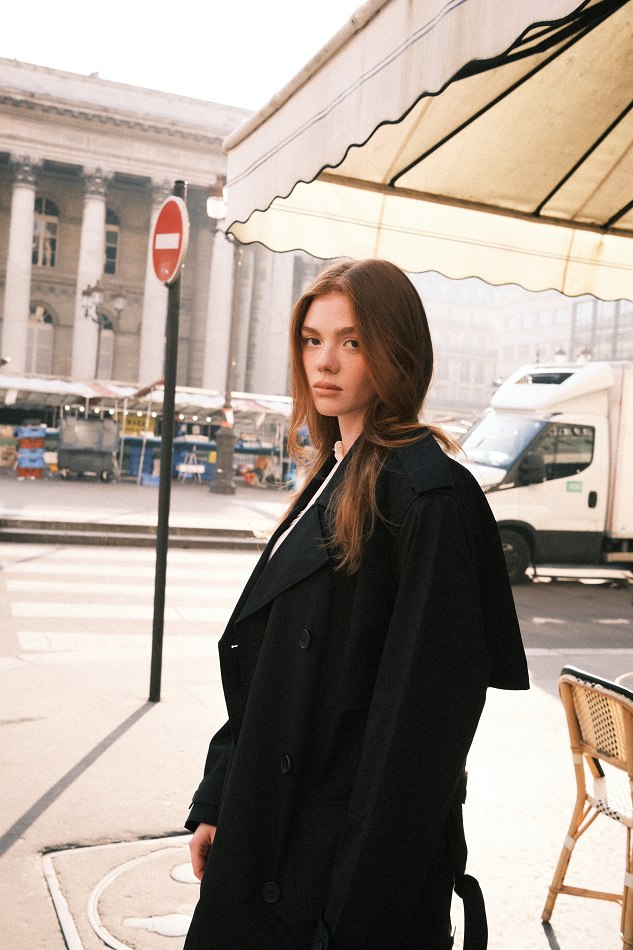 Camryn in a black coat on a sunlit city street